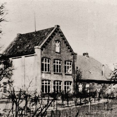 Die Alte Schule am Kirchplatz hatte zwei Klassenräume und zwei Lehrerwohnungen. Dazu rechts hinten ein Stall- Geräte- und Toilettengebäude.