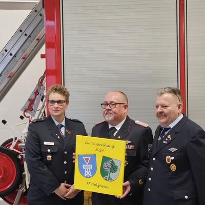 Bild vergr&ouml;&szlig;ern: Wehrführer Dirk Weber (rechts) und seine Stellvertreterin Sarah Kolter (links) aus der Partnergemeinde Holzheim überreichten Michael Wilkat zur Erinnerung an die Einweihung der neuen Feuerwache ein Bild.